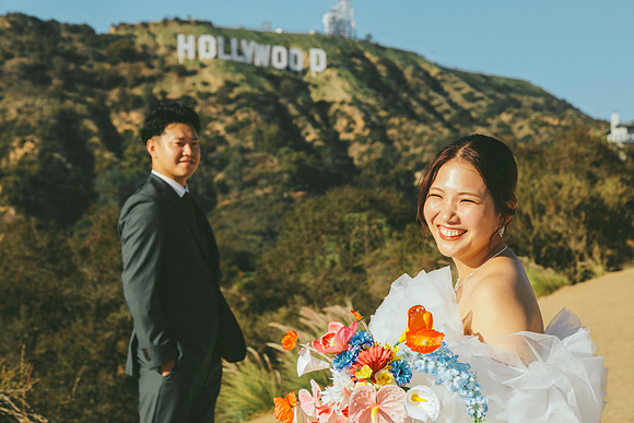 Bride and groom seen from behind looking toward the Hollywood Sign, with a colorful bouquet in the foreground.