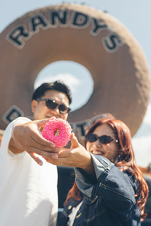 Couple holding a pink sprinkled donut in front of the Randy's Donuts sign in Los Angeles.