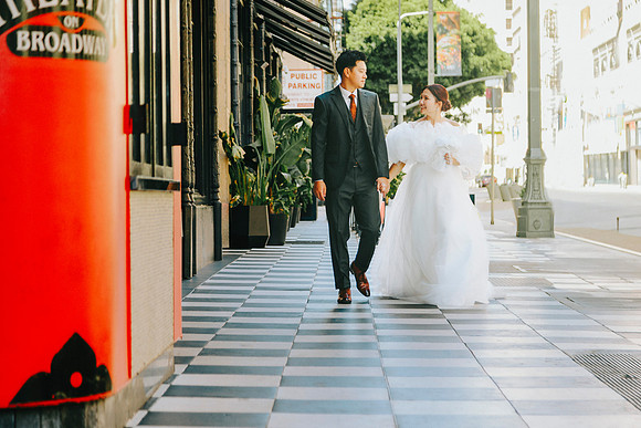 Bride and groom walking hand in hand on a black-and-white tiled sidewalk in Downtown Los Angeles.