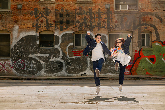 Couple jumping together in front of a graffiti-covered brick wall in Los Angeles.